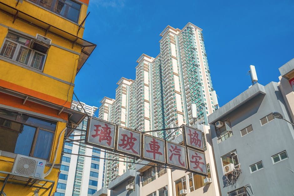 Low angle view of vibrant high-rise buildings in downtown Hong Kong under a clear blue sky.