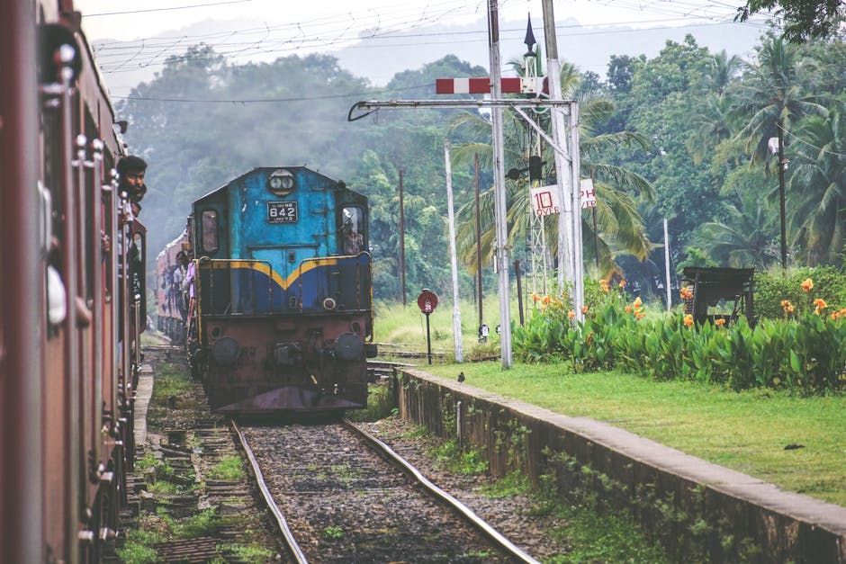 A vibrant train arriving at a scenic railway platform surrounded by greenery and flowers.
